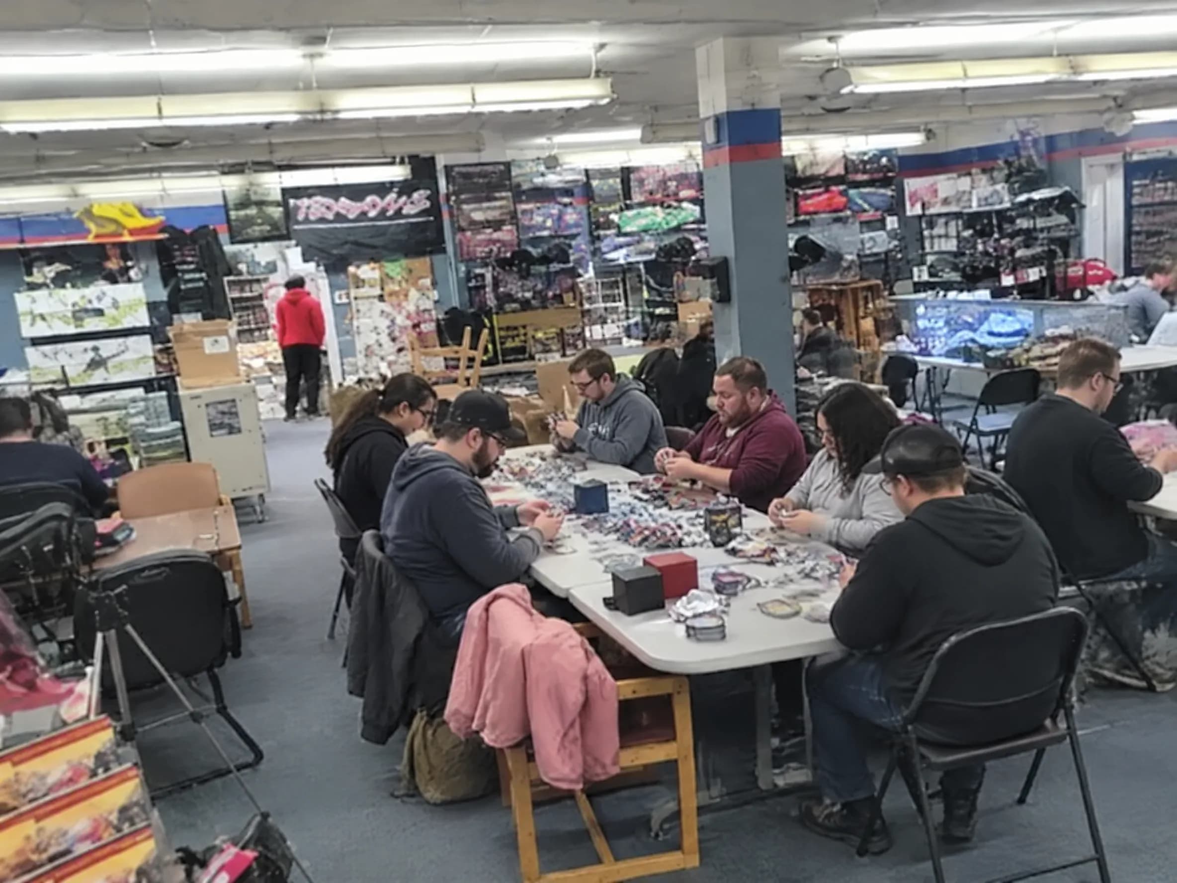Players opening booster packs at a long table for a draft.